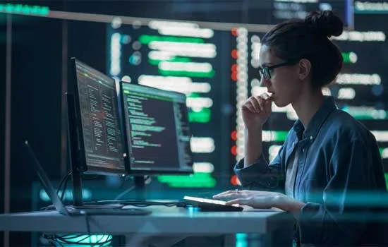 A Woman conducting software testing and coding in front of multiple computer screens and the backgroud is also shows lots of screens