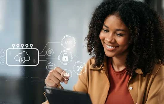 An african woman with curly hair smiles while using a tablet. Holographic tech icons, including a cloud and padlock, are displayed, suggesting cloud security. She is wearing khaki shirt