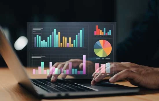 Hands typing on a laptop with colorful bar and pie charts floating above the screen. The image conveys a focus on data analysis and technology.