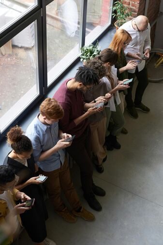 A group of Poople standing in a line and they are looking at their cell phones as if using the social media